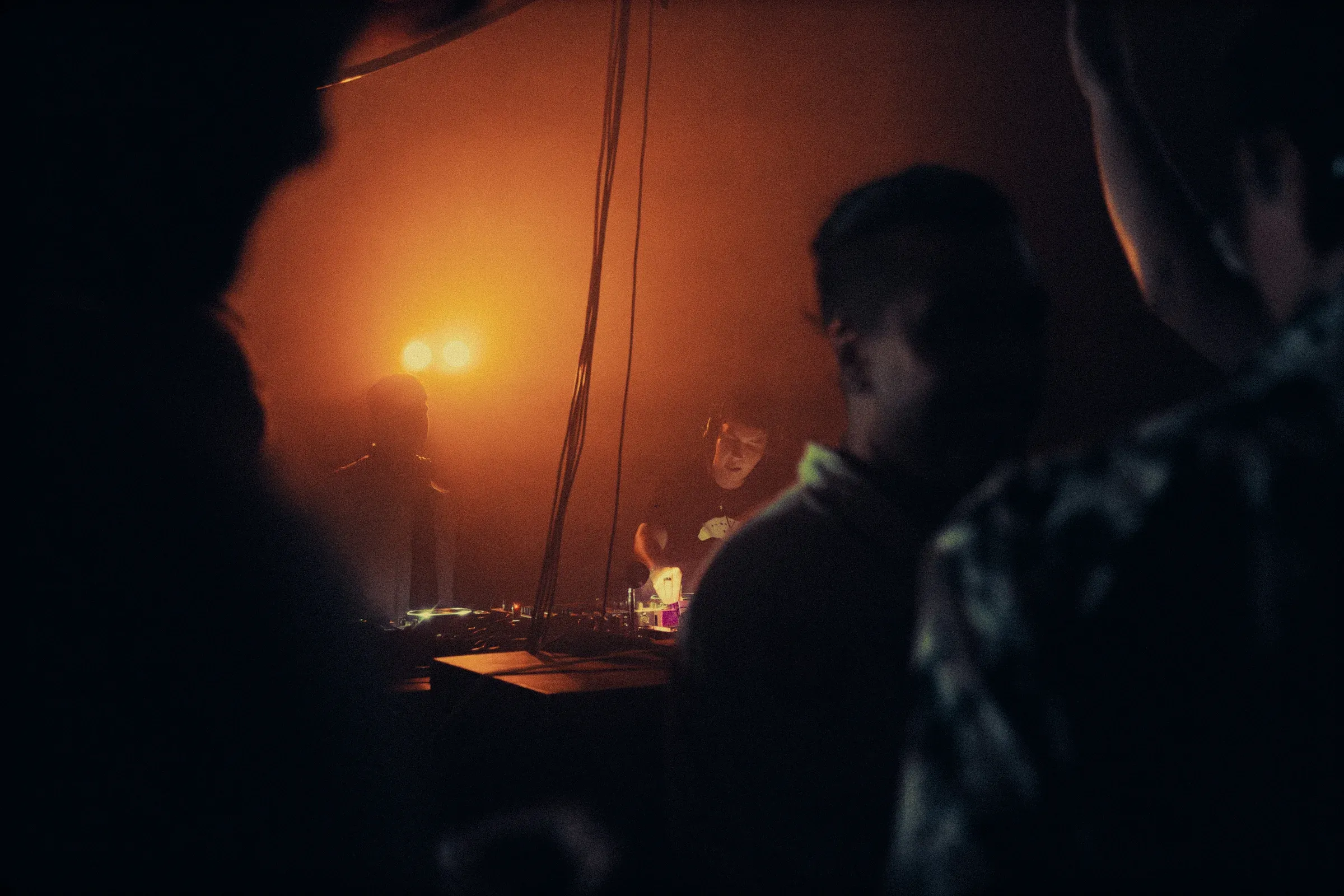 Público junto a la cabina del DJ iluminada en naranja